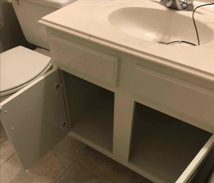 same corner of bathroom with vanity put back in, cabinets open