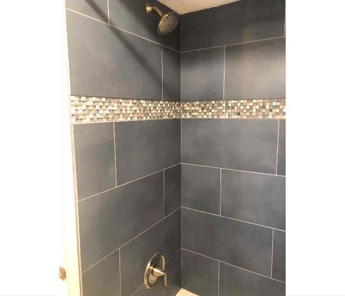 same area as before picture with walls rebuilt and grey-blue tile with new shower head and accent tile strip 3/4 way up