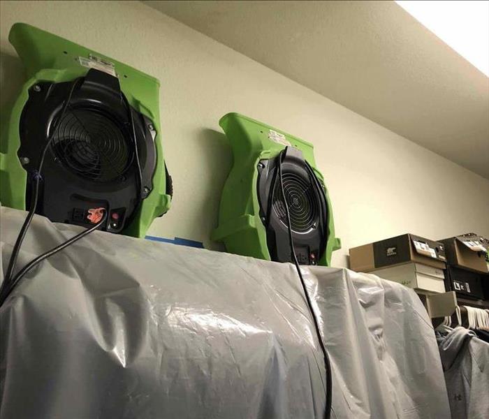 servpro fans on shelf drying out ceiling, shoe boxes and contents to the right, clothes hanging on rods