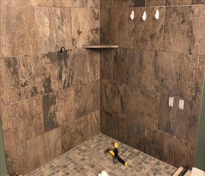 finished shower with tan tiles, shelf in the corner, and shower head at the top.