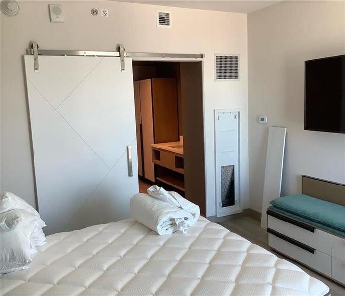 hotel room, sliding door to bathroom, dresser/couch located under mounted tv, bedding folded on bed, panel off wall