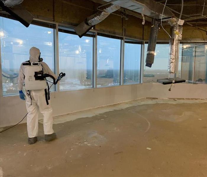 Commercial building with man in full PPE gear with fogging backpack, fogging the area