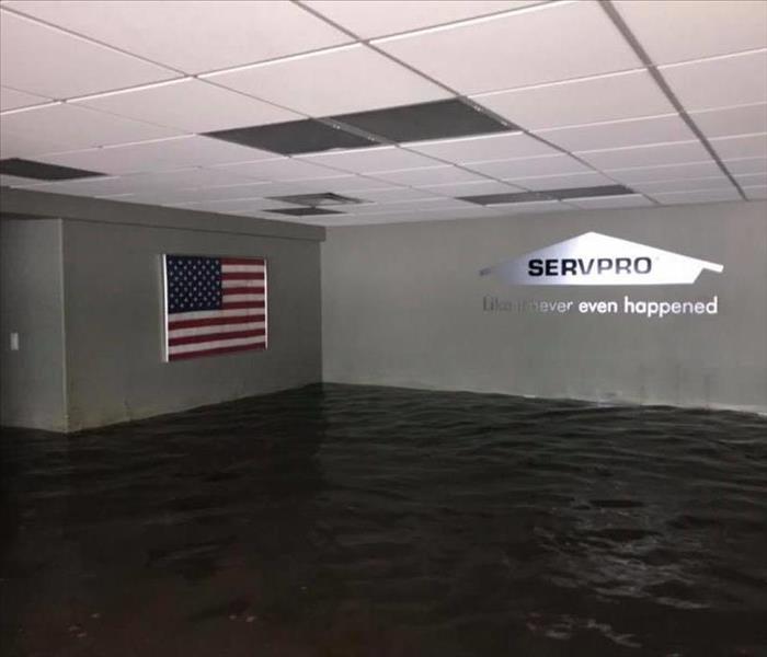 building with water almost up to the ceiling, SERVPRO house on right wall, American flag on left wall