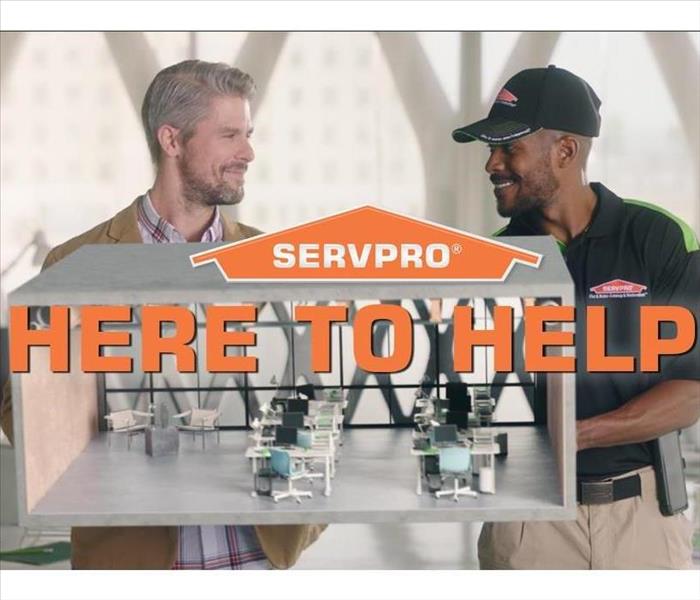 two men looking at each other laughing, one professionally dresses, one dressed in SERVPRO uniform. "here to help" SERVPRO