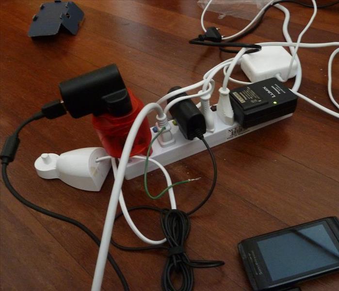 Power strip with a lot of cords plugged into it and the wires are all tangled up sitting on the floor